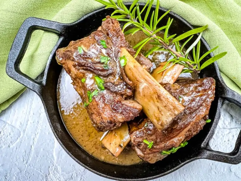 Garlic braised short ribs on a black platter, garnished with herbs.