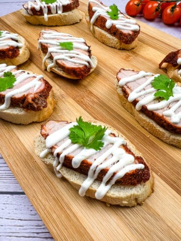 spicy pork tenderloin crostini with lime crema on a wooden platter