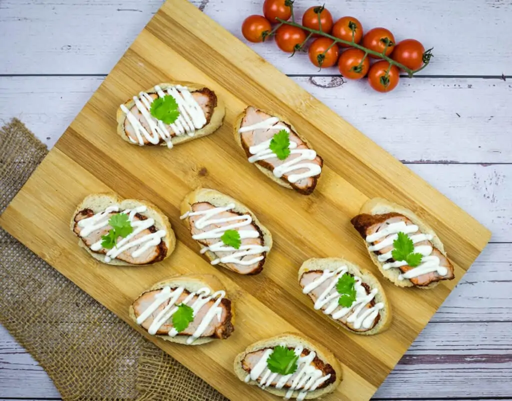 Spicy Pork Tenderloin Crostini with Lime Crema on a wooden platter.