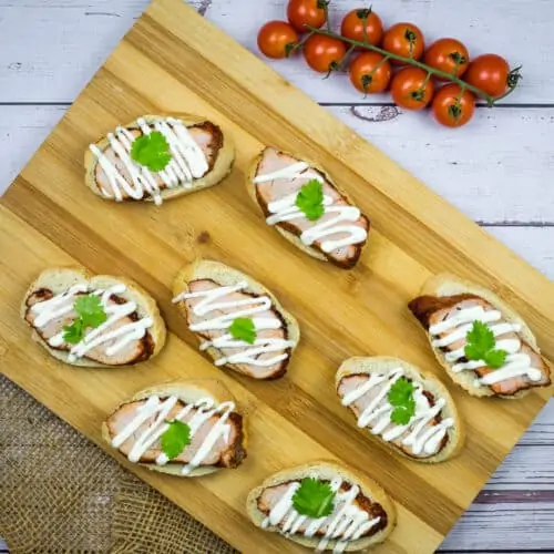 Spicy Pork Tenderloin Crostini with Lime Crema on a wooden platter.