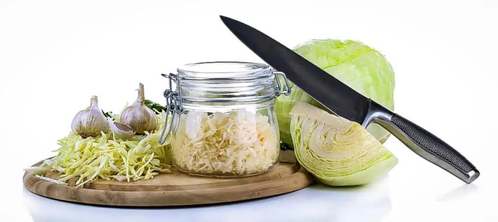 A knife poised above a cutting board, ready to slice through a vibrant sauerkraut with apples & bacon mixture.