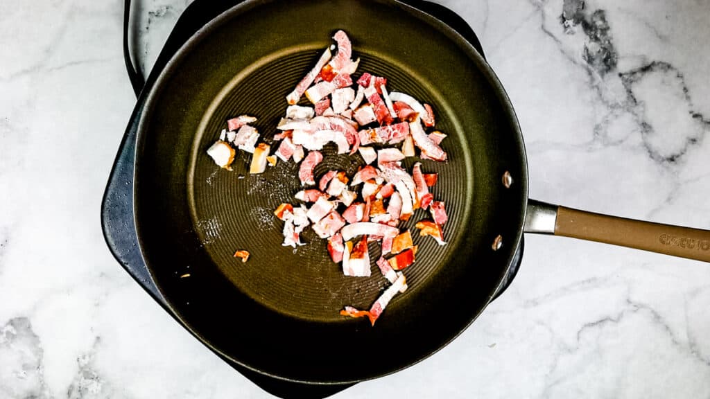 Cooking bacon in a skillet to make sauerkraut with apples and bacon.
