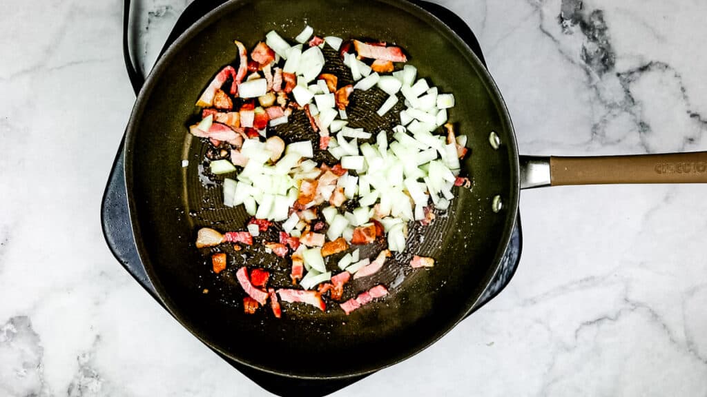 Adding the onion to the bacon and rendered fat in a skillet.