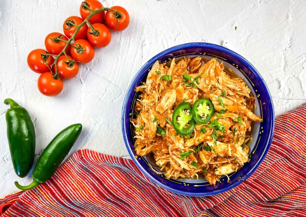 Instant Pot Mexican chicken tinga in a blue bowl with tomatoes and jalapenos.