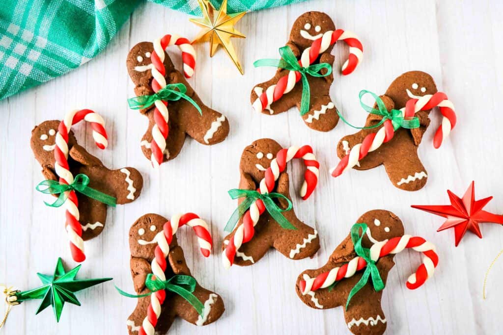 Several chocolate gingerbread cookies holding candy canes on a white table.