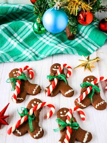 5 chocolate gingerbread men with candy canes with a small christmas tree in the background