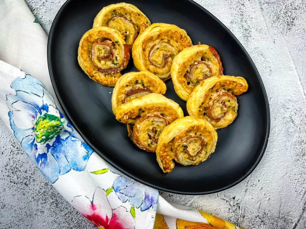 parmesan and prosciutto puff pastry pinwheels on a black platter