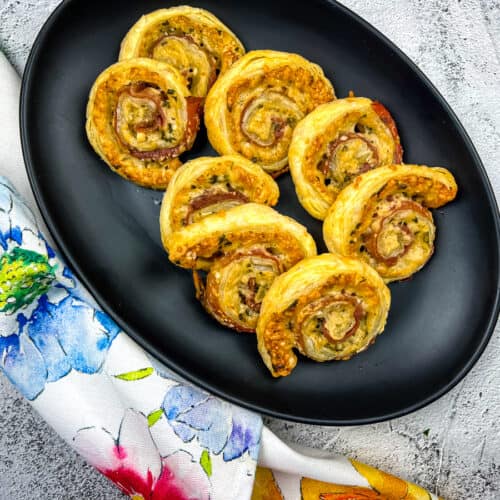 Parmesan and prosciutto puff pastry pinwheels on a black platter.
