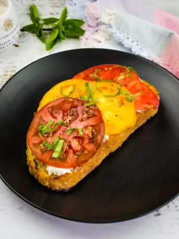 grilled bread with tomato and ricotta on a black plate