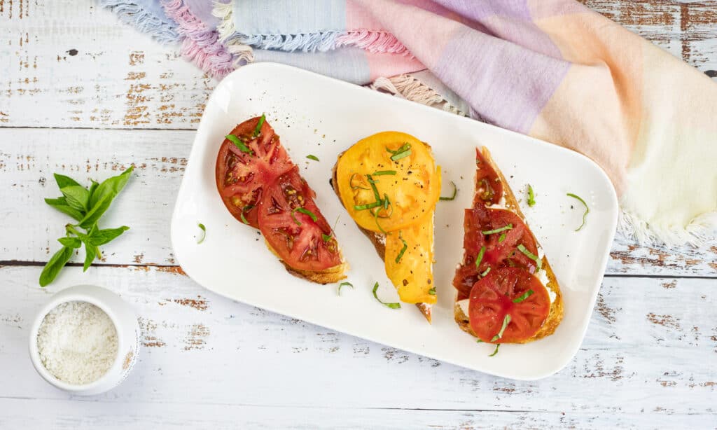 Grilled bread with tomatoes and ricotta, sprinkled with fresh basil on a plate.