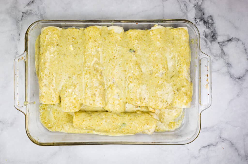 Smoked chicken enchiladas in a casserole dish topped with sauce.