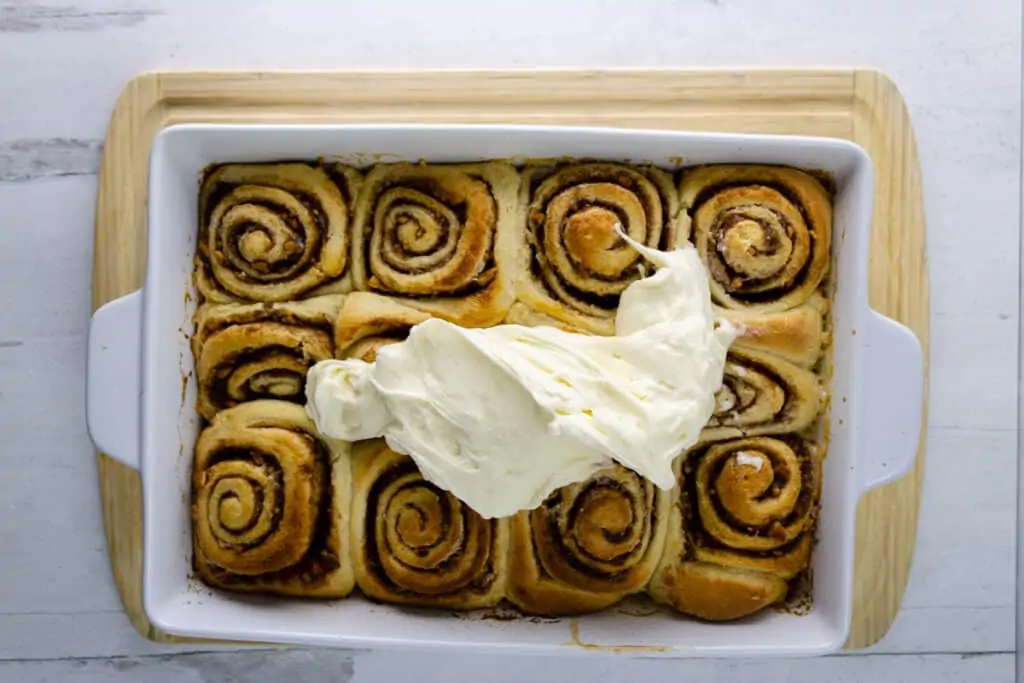 Baked apple pie cinnamon rolls in a baking dish topped with cream cheese frosting.