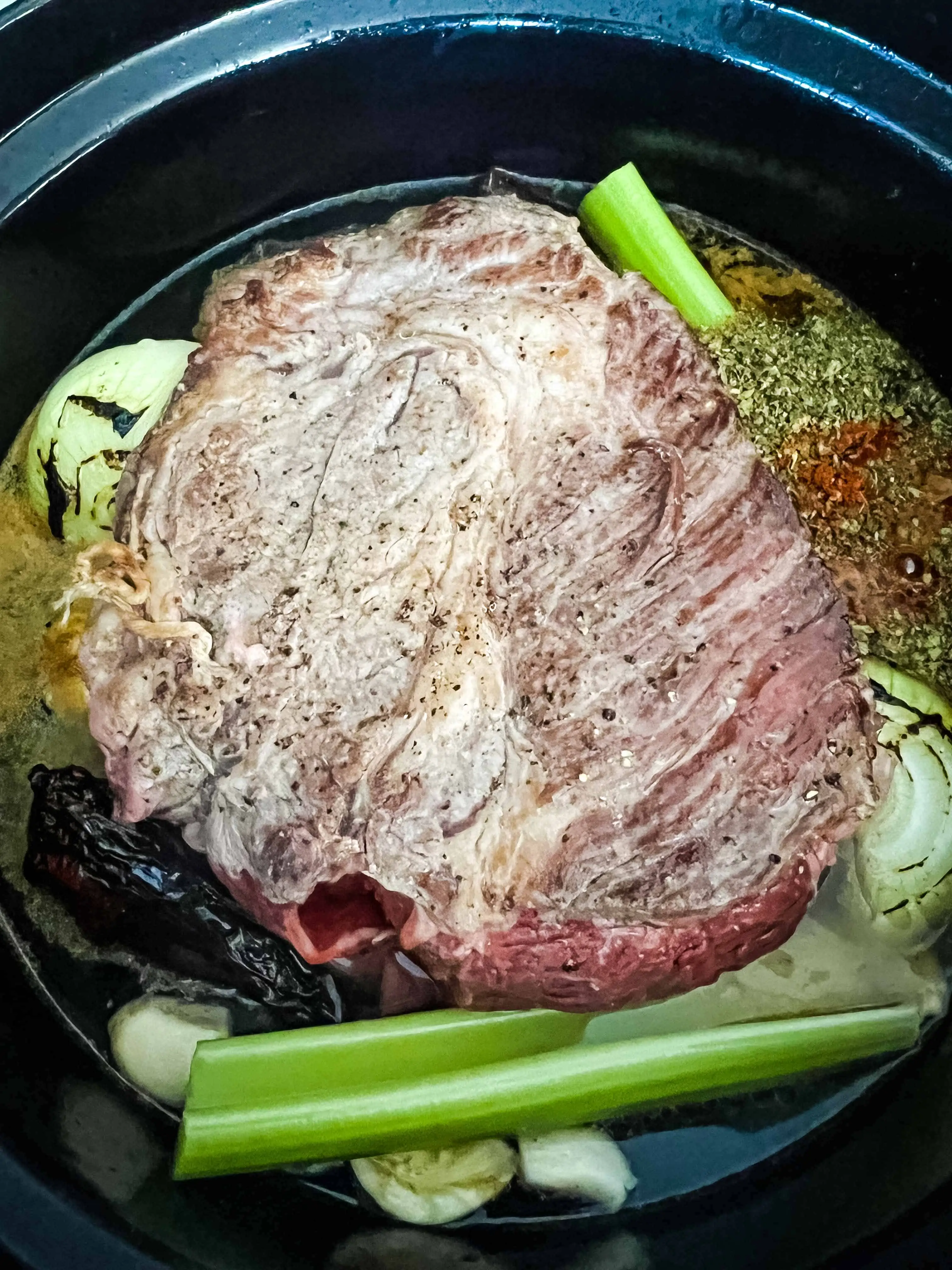 beef, vegetables, chilis and broth in the dutch oven ready for braising.