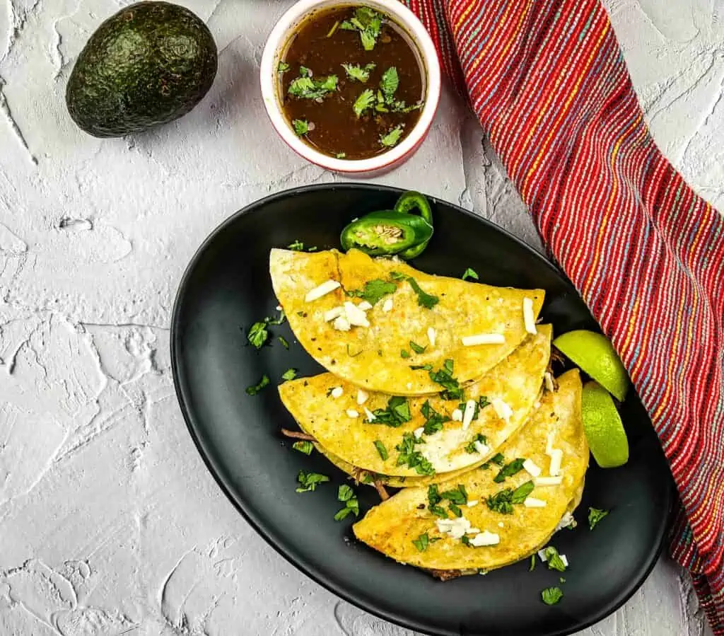 birria tacos and broth on a black plate