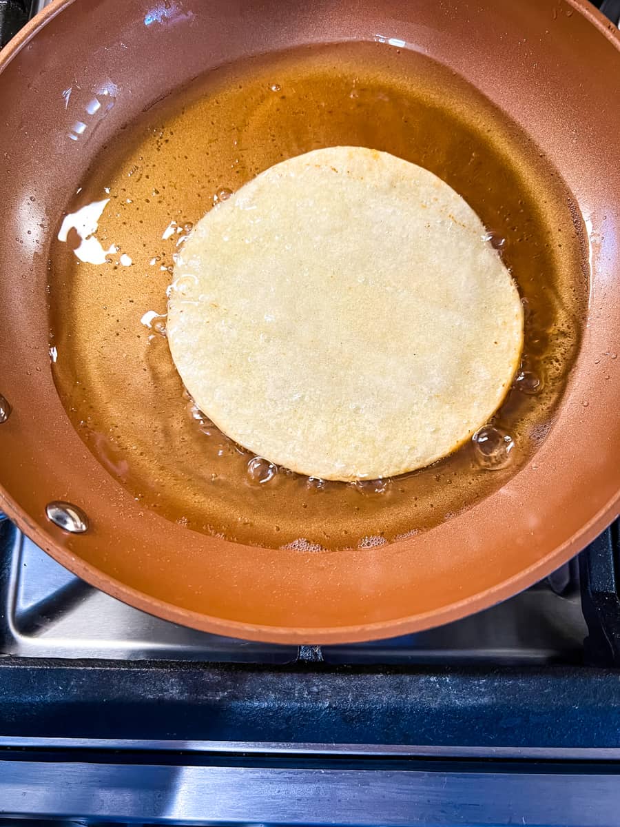 a corn tortilla frying in oil in a skillet to make chicken tinga tacos