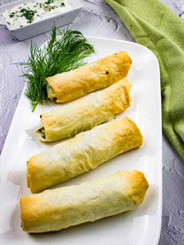 spanakopita rolls on a plate with dill and tzatziki