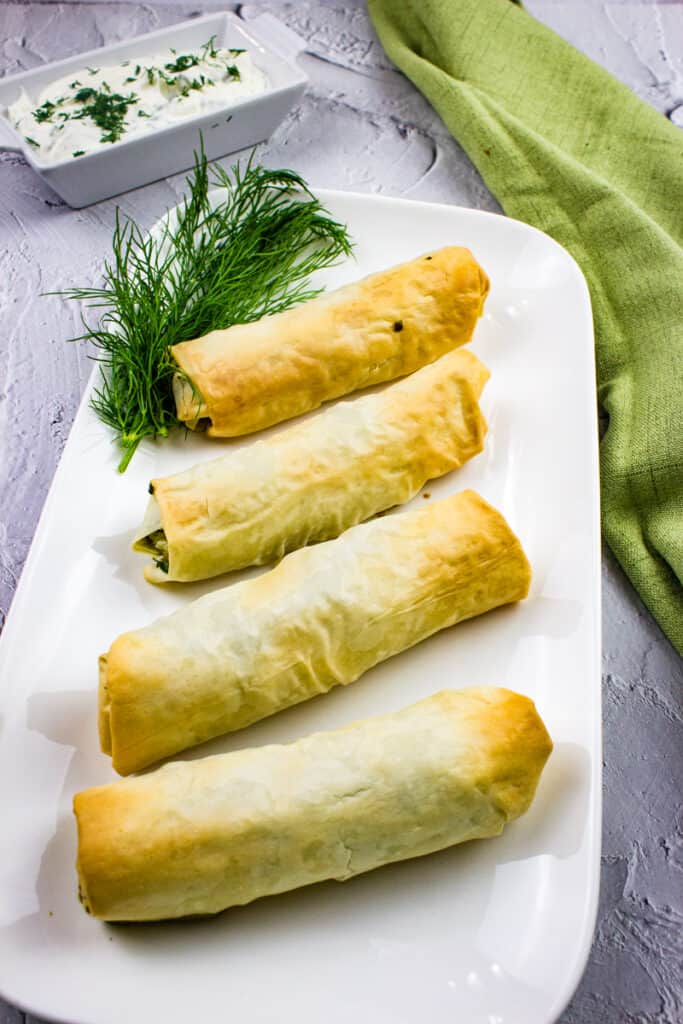 spanakopita rolls on a plate with dill and tzatziki