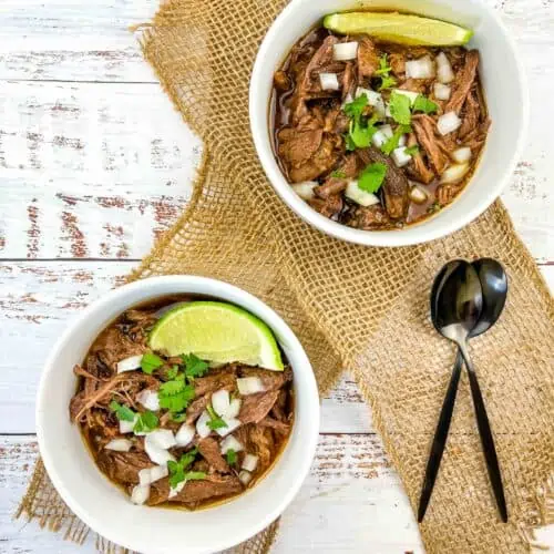 two servings of birria de res in bowls with lime
