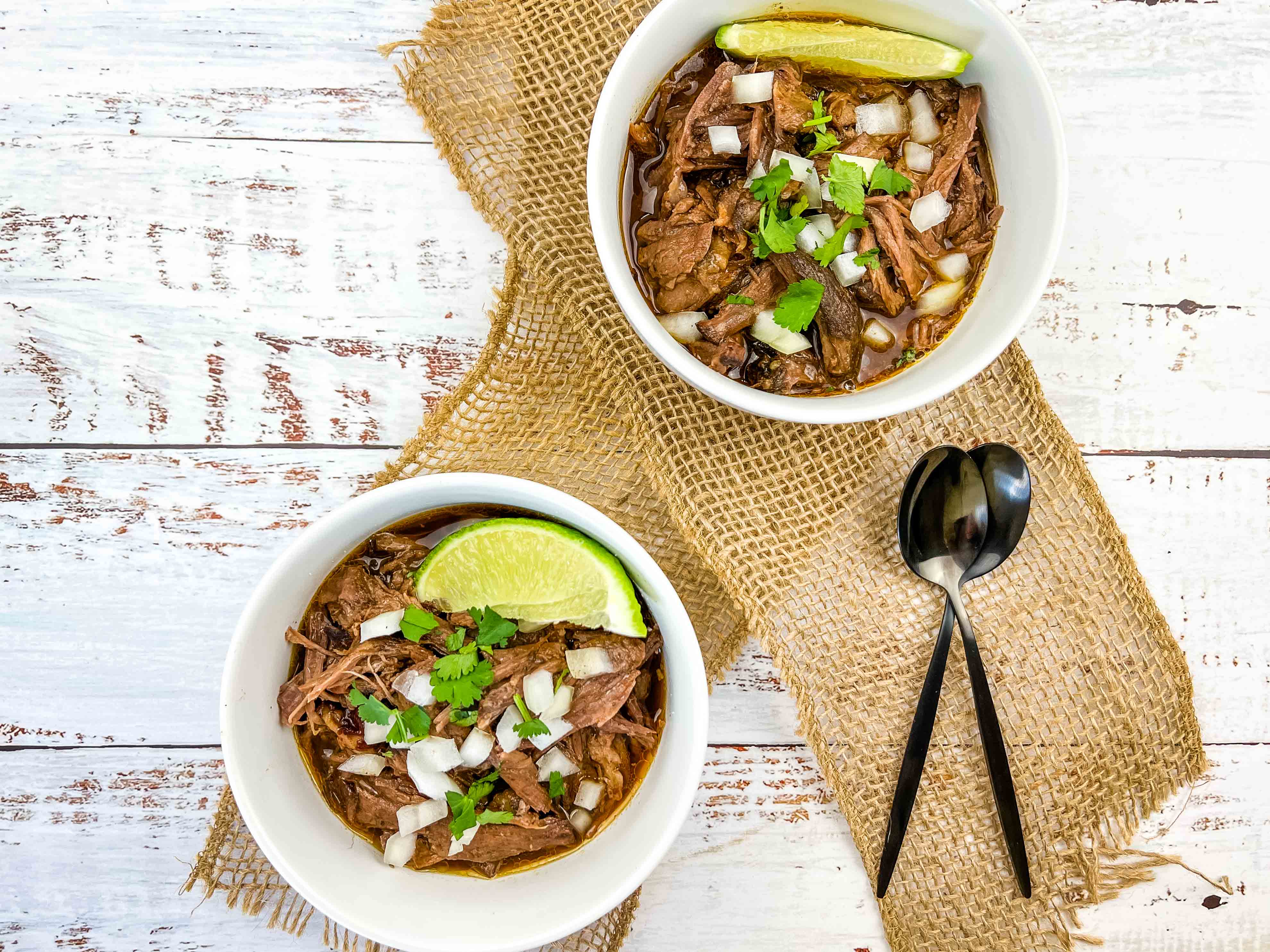two servings of birria de res in bowls with lime
