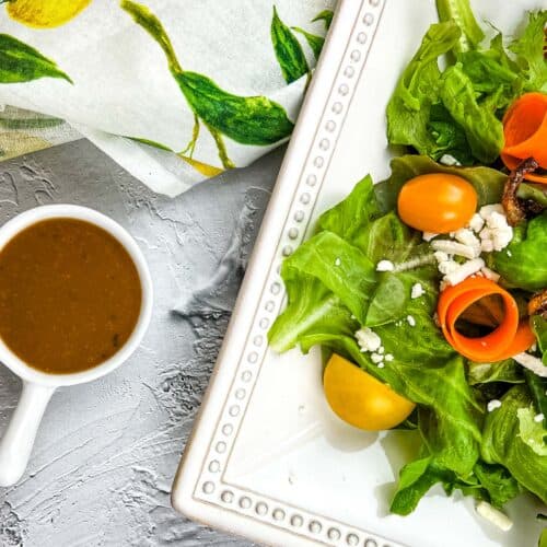 A cup of creamy balsamic vinaigrette and a plate of salad beside it.