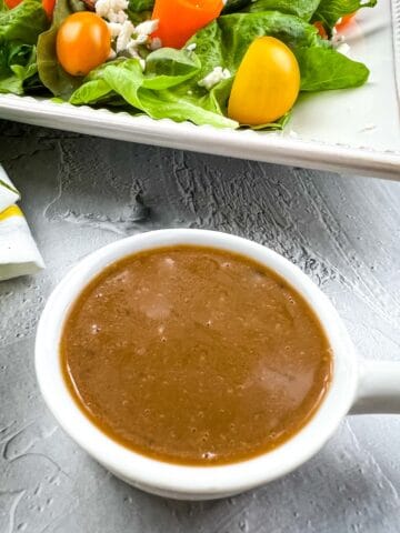 Creamy balsamic vinaigrette in a bowl with a salad in the background.