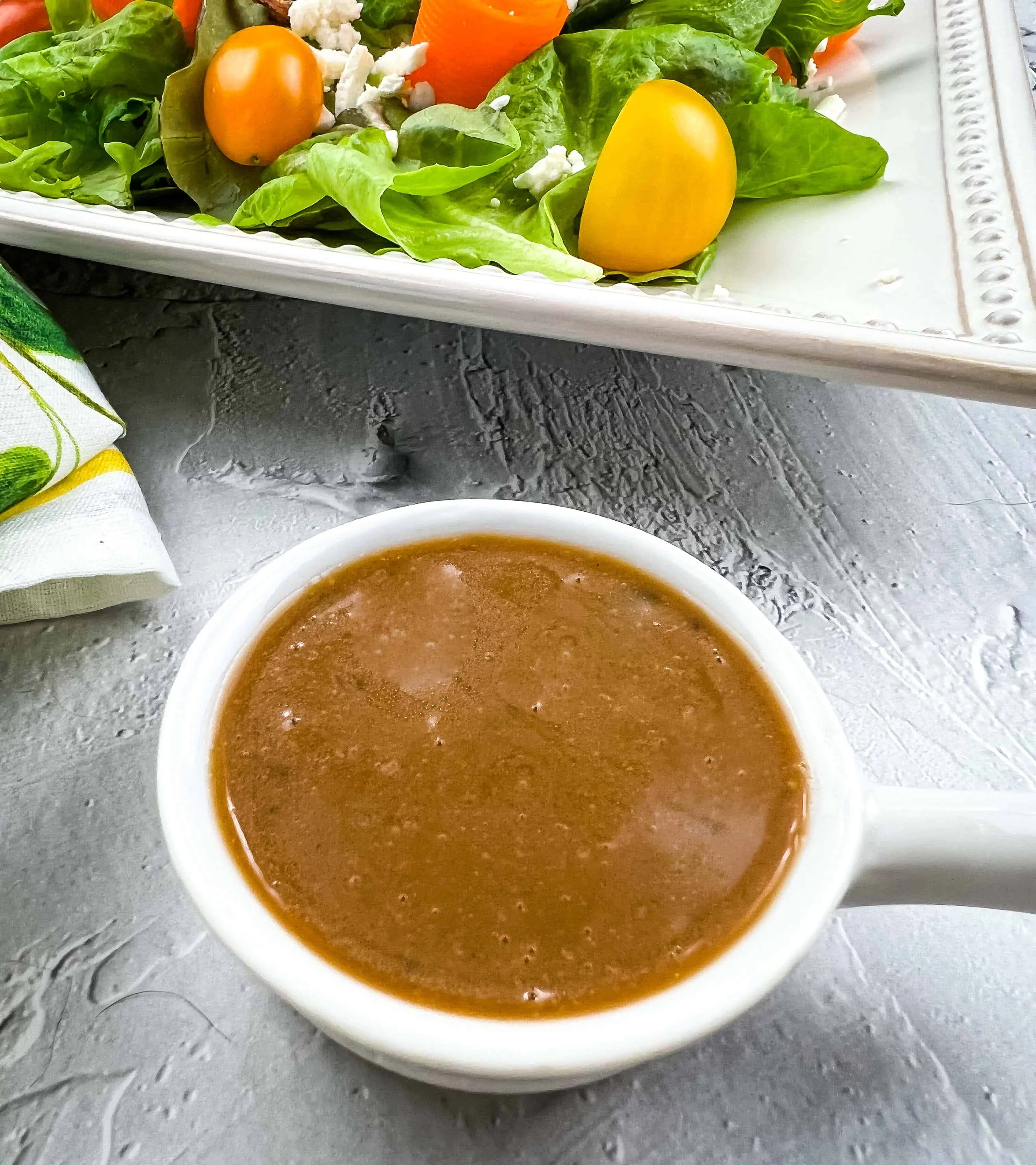 Creamy balsamic vinaigrette in a bowl with a salad in the background.