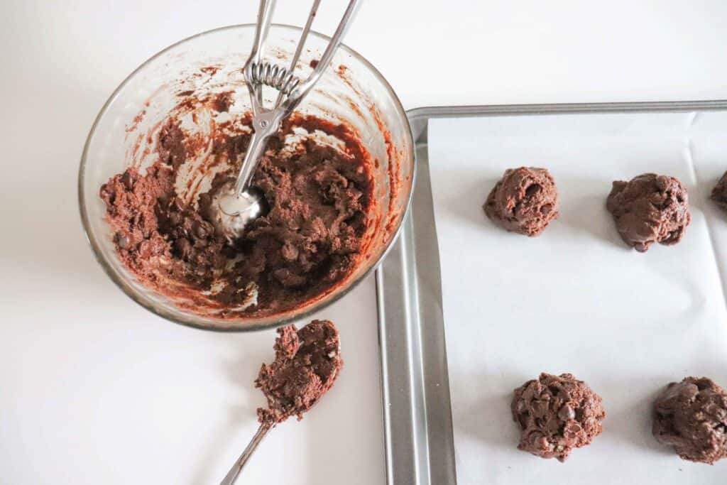 Scooping cookies onto a parchment paper lined baking sheet.