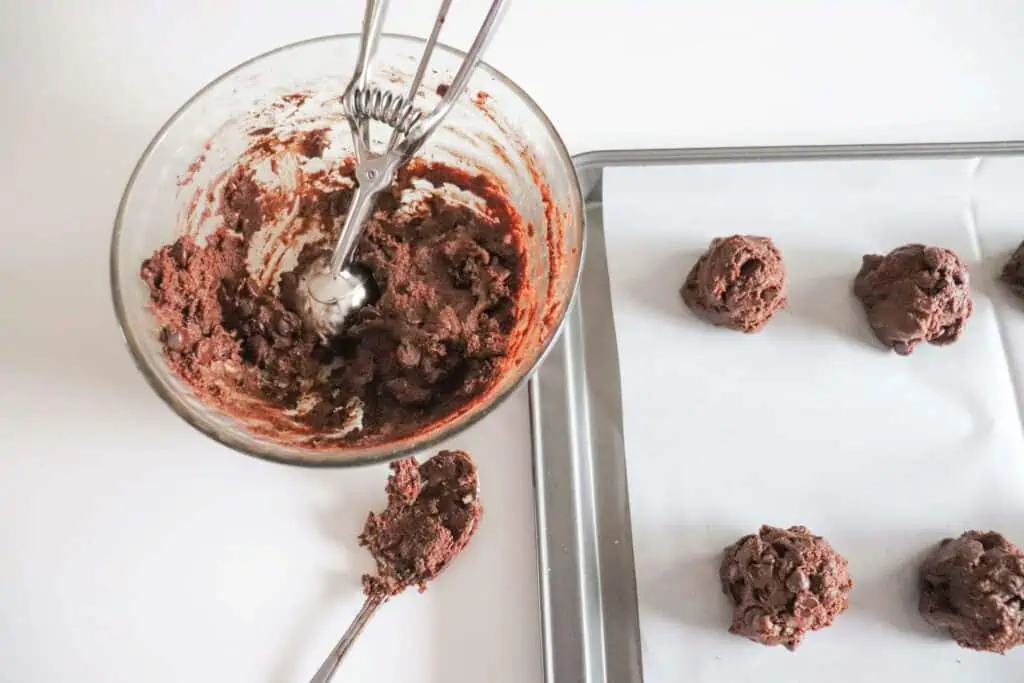 Scooping cookies onto a parchment paper lined baking sheet.