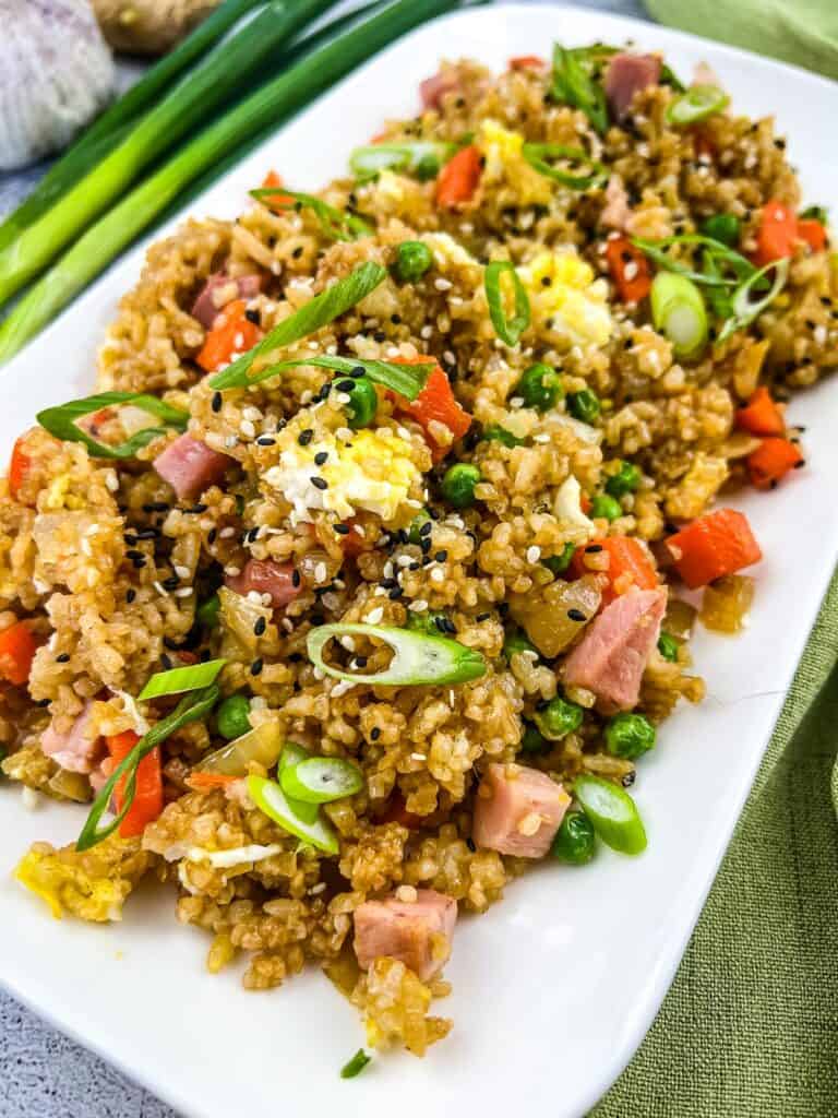 Ham fried rice garnished with green onions on a white platter.