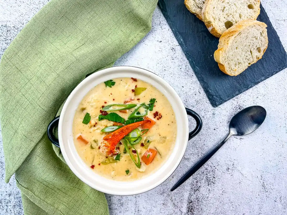 A bowl of lobster chowder with bread on the side.