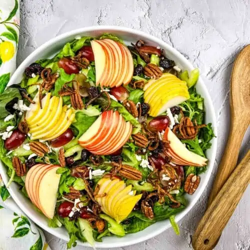 waldorf salad in a large bowl with serving spoons on the side