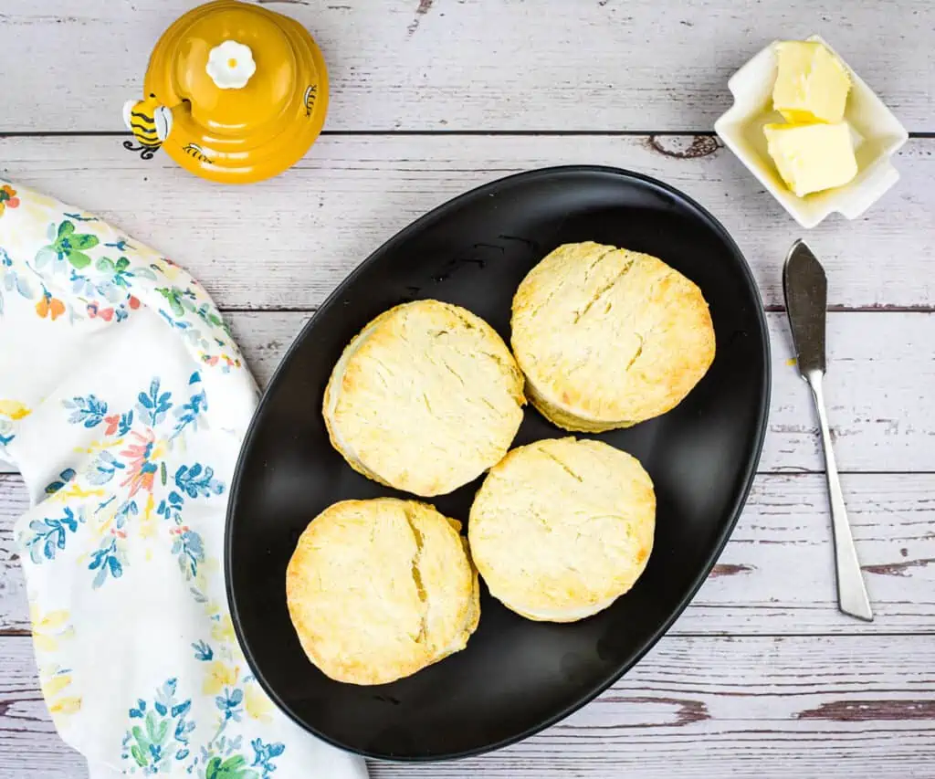 Finished smoked biscuits on a black plate with butter and honey in the background.