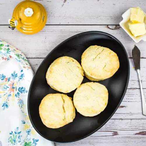 Finished smoked biscuits on a black plate with butter and honey in the background.
