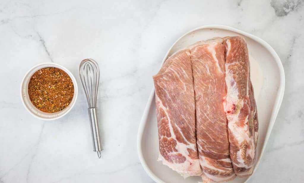 the carnitas pork rub in a bowl next to the raw pork