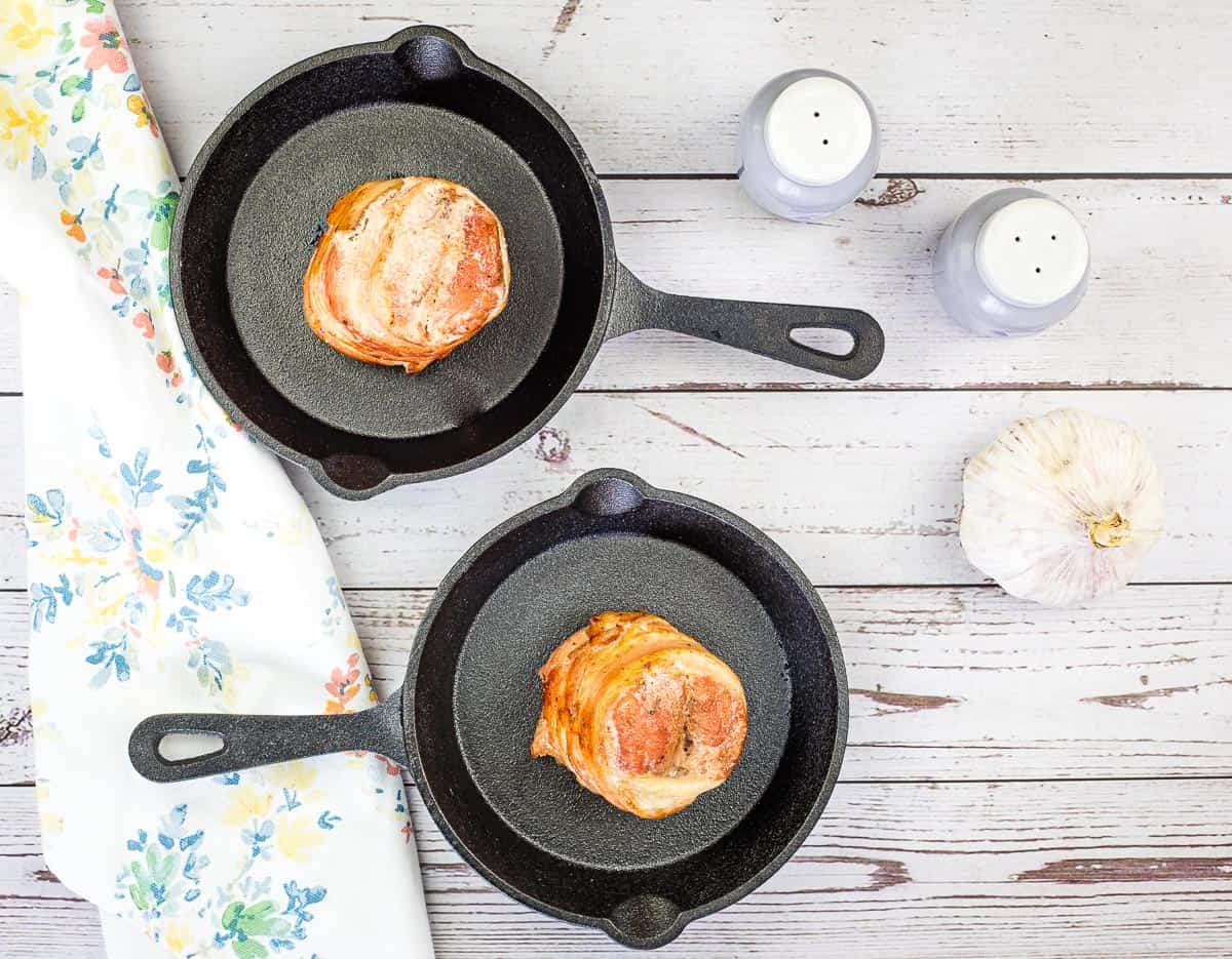 Two smoked bacon-wrapped pork tenderloins in skillets.
