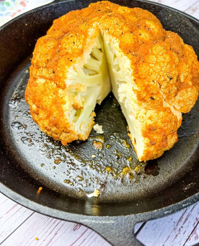 smoked cauliflower in a cast iron dish with a wedge cut out of it