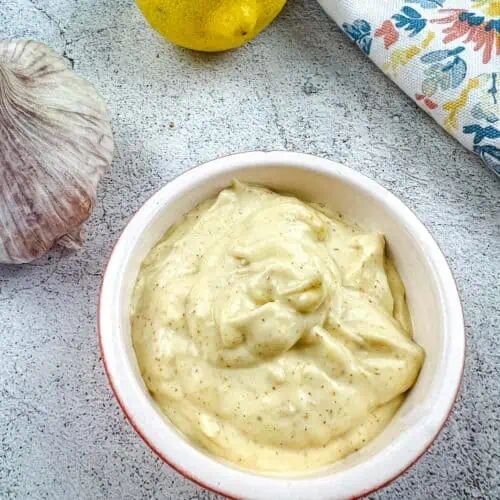 spicy garlic aioli in a bowl with lemon and garlic in the background