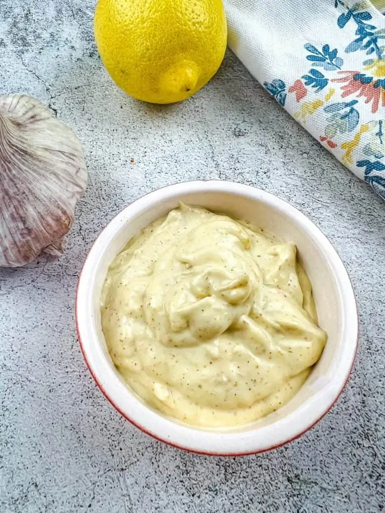 spicy garlic aioli in a bowl with lemon and garlic in the background