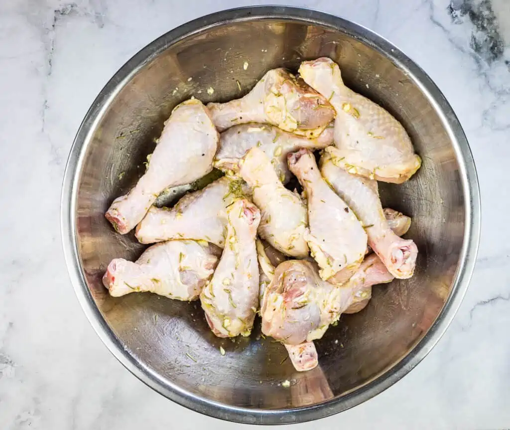 tossing raw chicken legs with seasoning in a large bowl