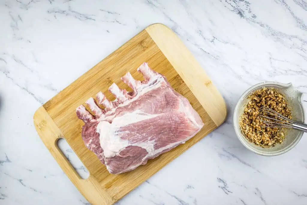 raw rack of pork next to a bowl of the garlic rub.