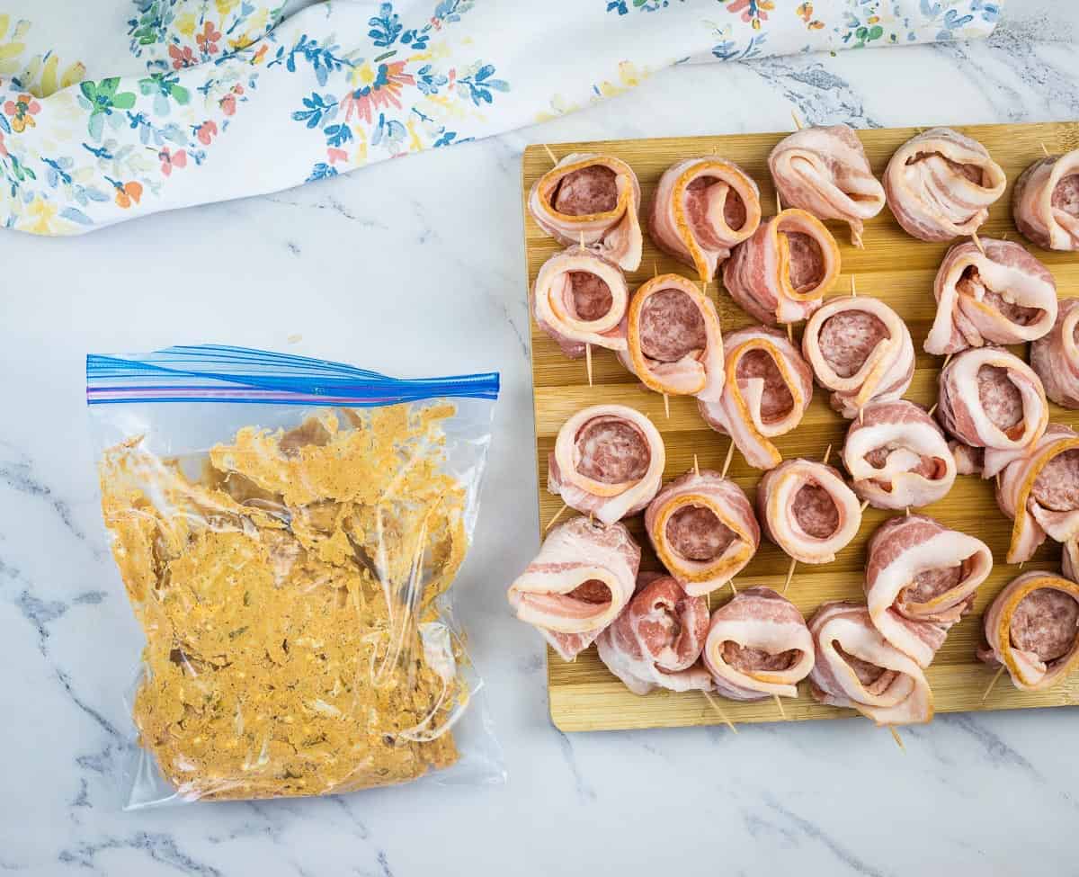 bacon wrapped sausage on a board with the filling in a bag