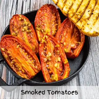 smoked tomatoes on a black plate with grilled bread on the side.