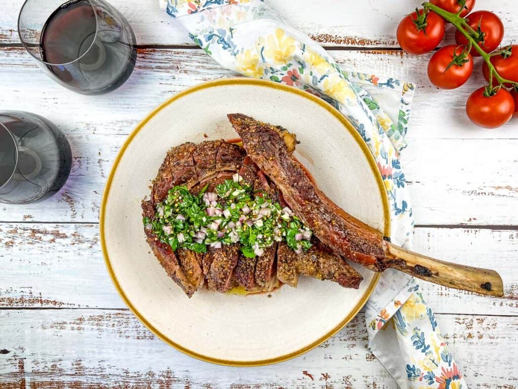 smoked tomahawk steak topped with mustard seed chimichurri on a plate