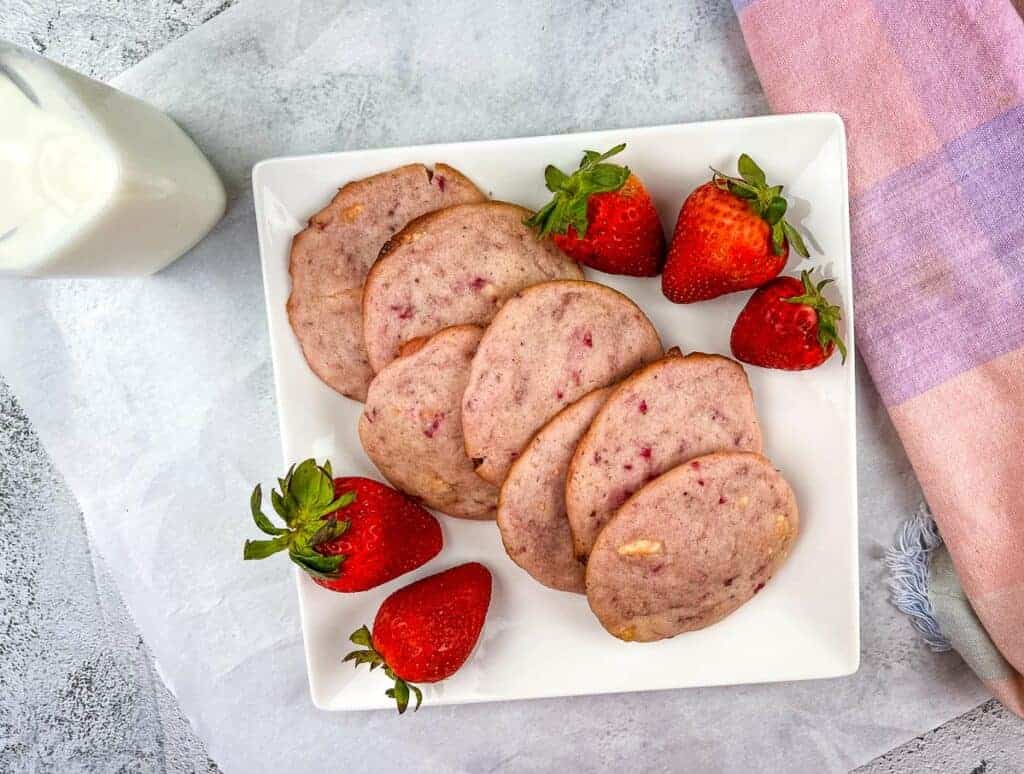 Strawberry shortcake cookies arranged on a plate next to a glass of milk.