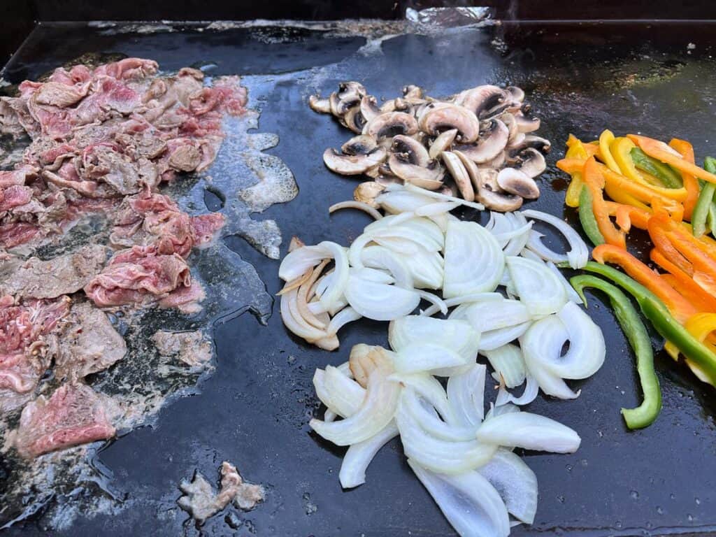 the meat and veggies cooking on the blackstone