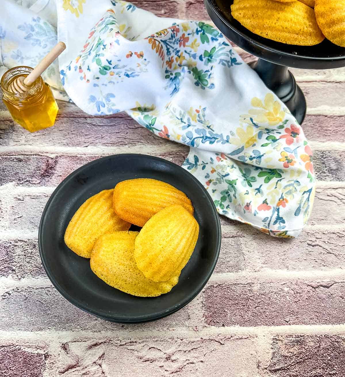 honey butter cornbread madeleines on a black plate with honey in the background
