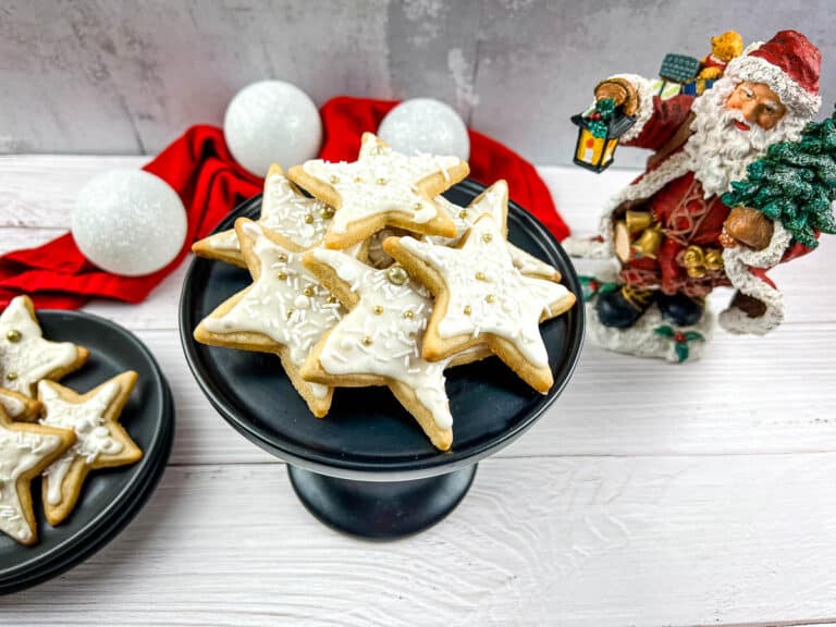 Santa claus figurines surrounding a plate of eggnog sugar cookies.