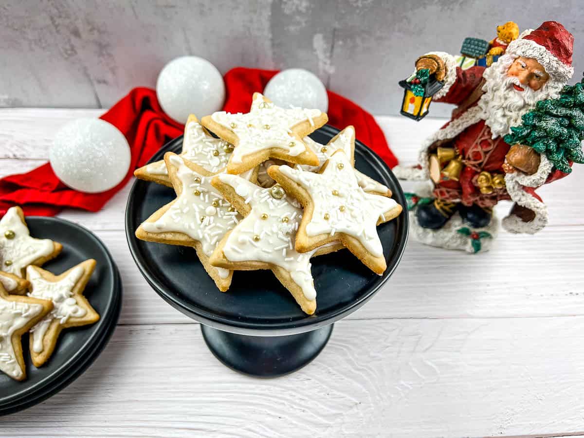 Eggnog sugar cookies on a plate with santa claus figurines.