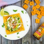 cheez-it tostada on a plate with crackers and hot sauce nearby
