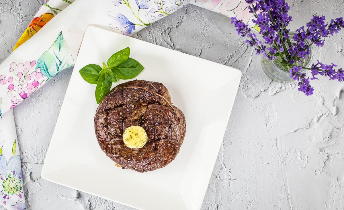 A top-down shot of Grilled Ribeye Cap Steak on a cutting board with veggies.